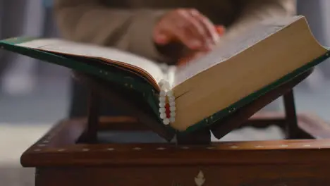 Close Up Of Muslim Woman Praying Putting Prayer Beads Into Copy Of The Quran At Home