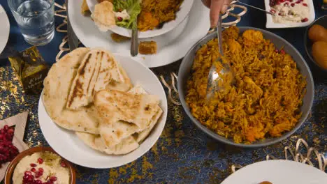 Close Up Of Muslim Family Sitting Around Table With Food For Meal Celebrating Eid Being Served 3