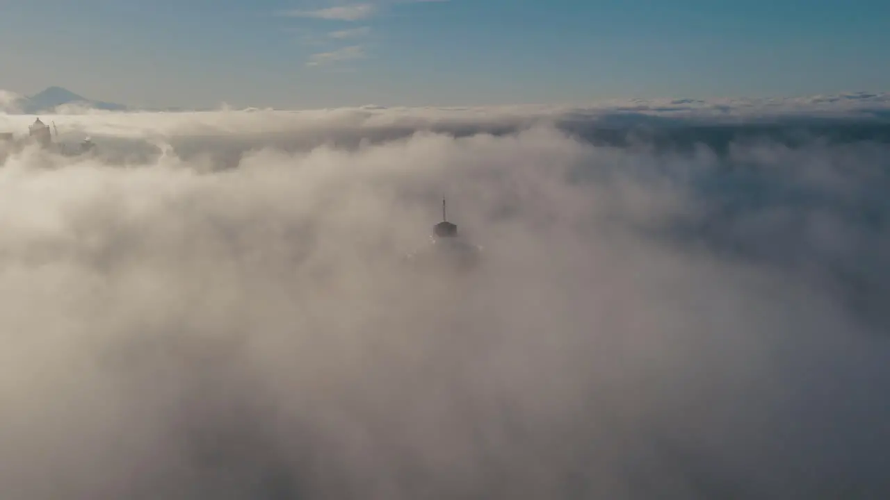 Drone descends in sky above fog to reveal upper level platform of iconic building with Mt