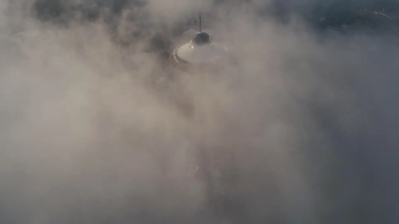 Static establishing overview of iconic tower immersed in flowing fog with dreamy light dancing in mist