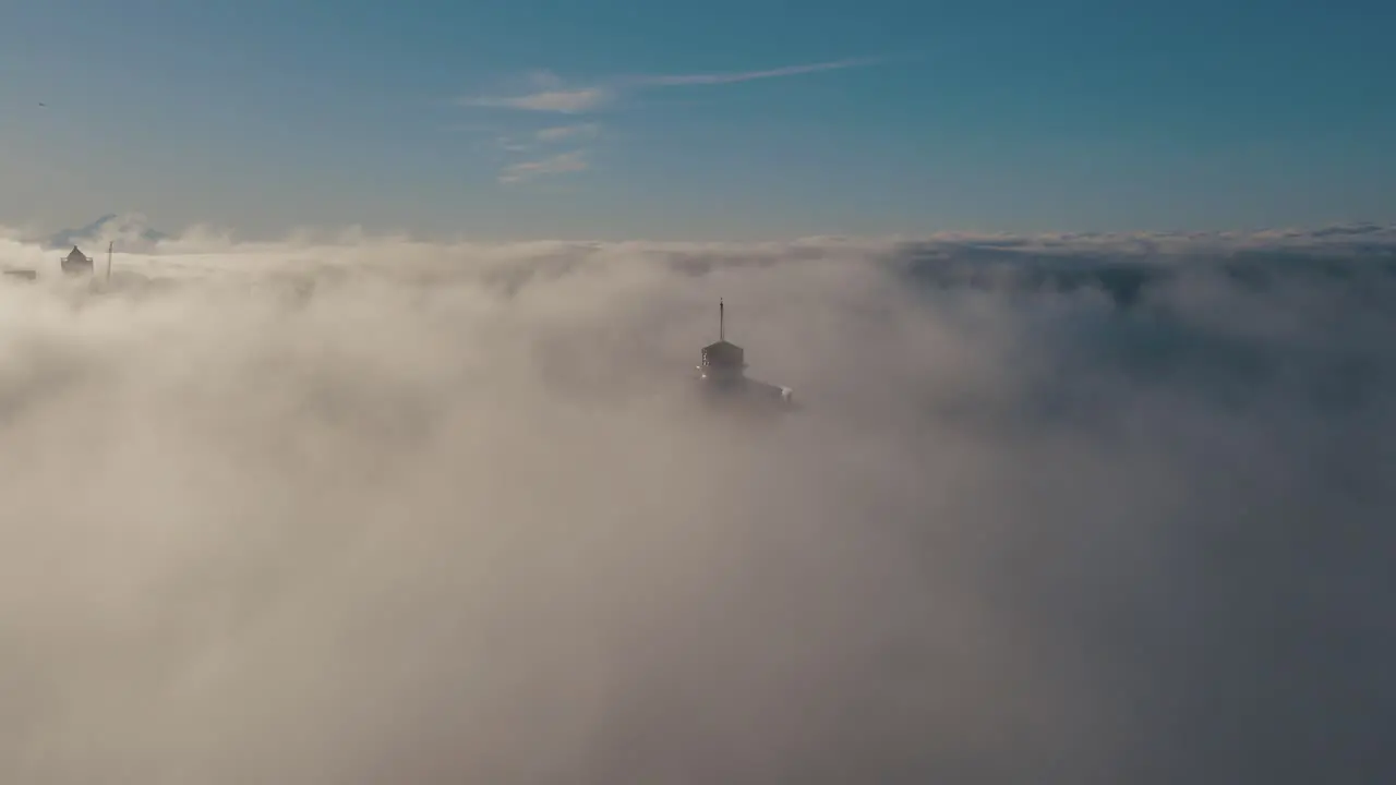 Top needle of historic building pokes past dense thick layer of fog drone pullback ascend