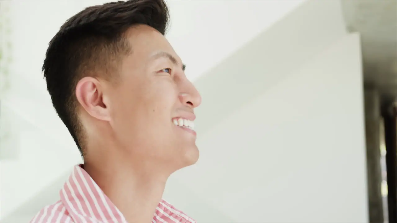 A young Asian man smiles brightly at home in a well-lit space with copy space