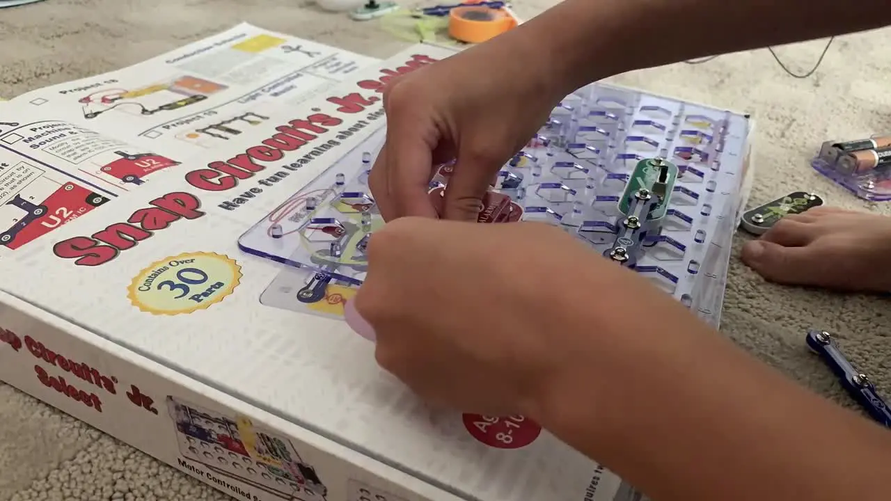 A time lapse video of small hands busily putting together snap circuits on the plastic board to create sound and light