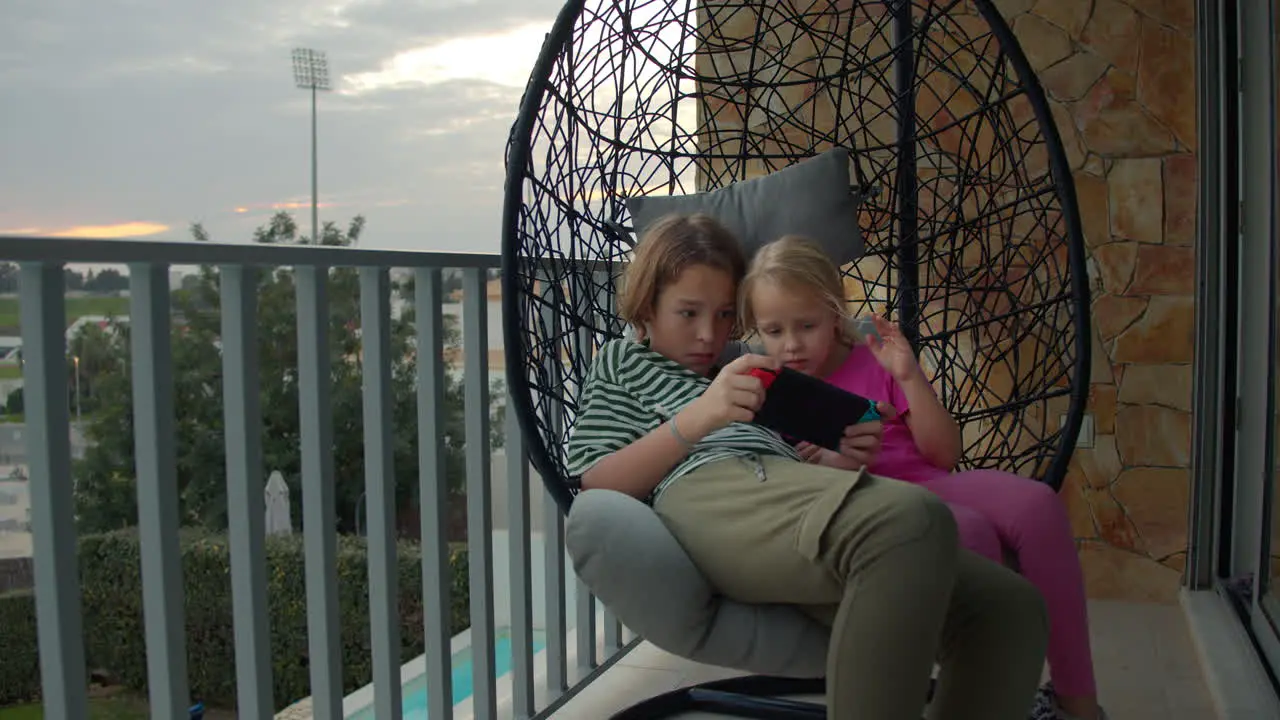 Siblings playing video games on swing chair