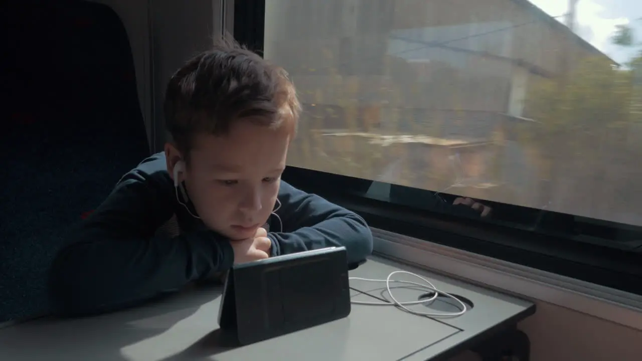 Kid with earphones watching cartoon on cell in train