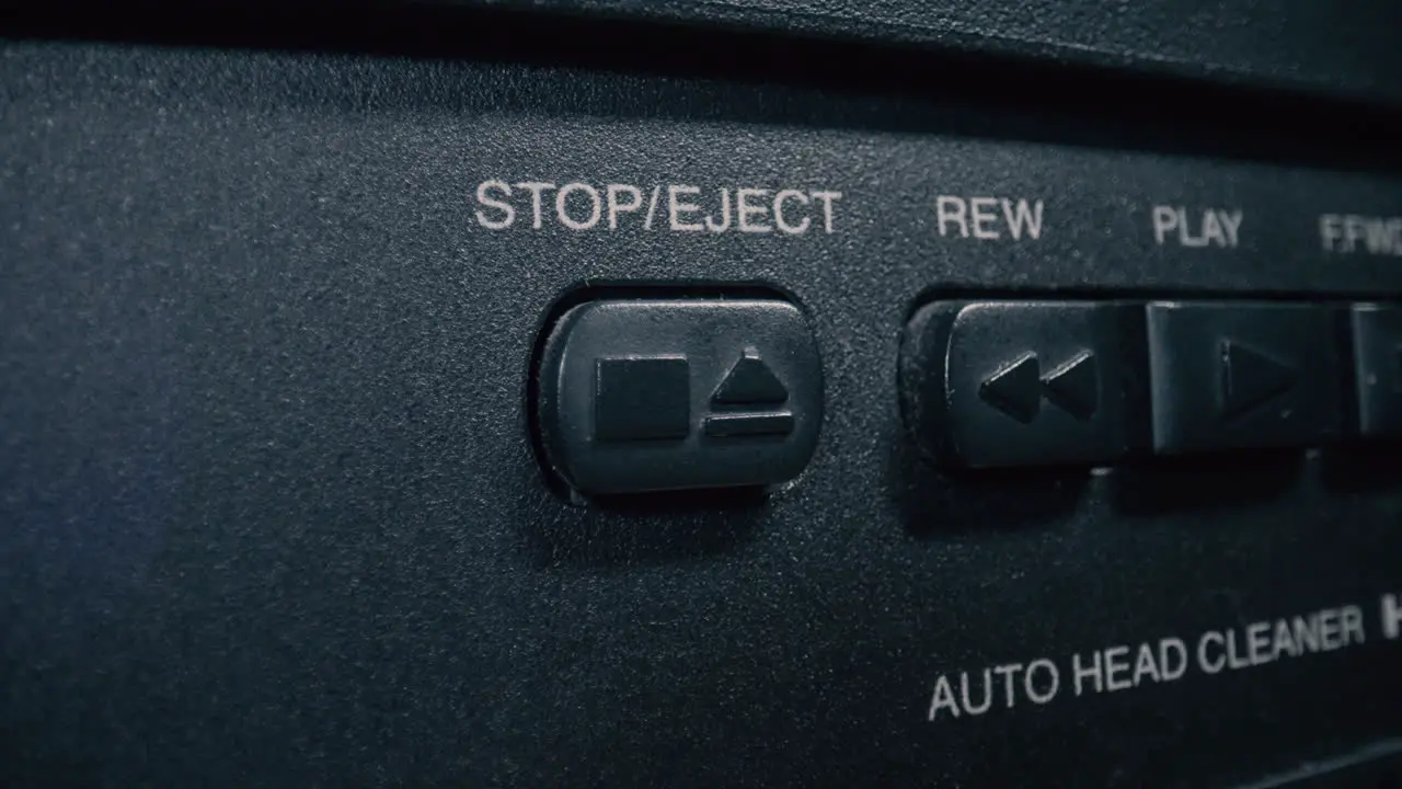 Close-up macro shot of a finger pressing the 'stop' button on a vintage VCR player's control panel