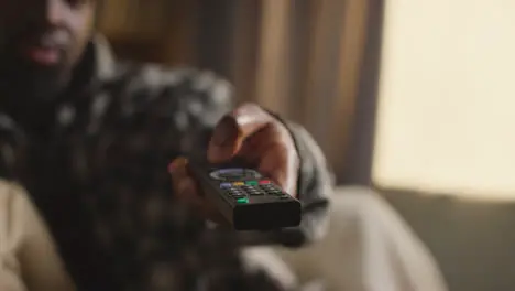 Close Up Of Man Relaxing At Home Sitting On Sofa Changing TV Channels With Remote Control