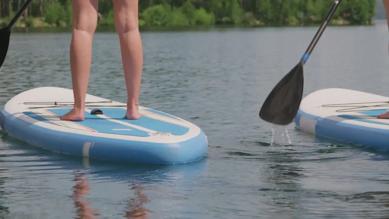 Camera Focuses The Legs Of Two Girls Who Are Paddling With The Board And The Oars In The Water