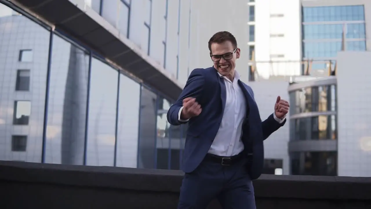 Front View Of Young Businessman Looking Around To Sure Noone See Him And Starts To Express His Feeling About Victory And Big Success On The Street Near The Office Center Wearing Suit Celebrating His Achievements