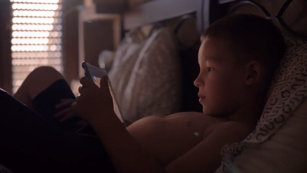 Child lying in bed and watching cartoon on tablet computer