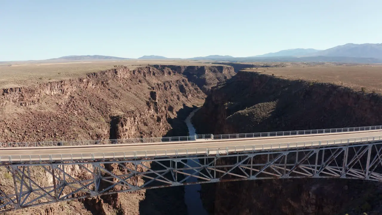 Aerial as semi truck drives over deep desert canyon on large bridge