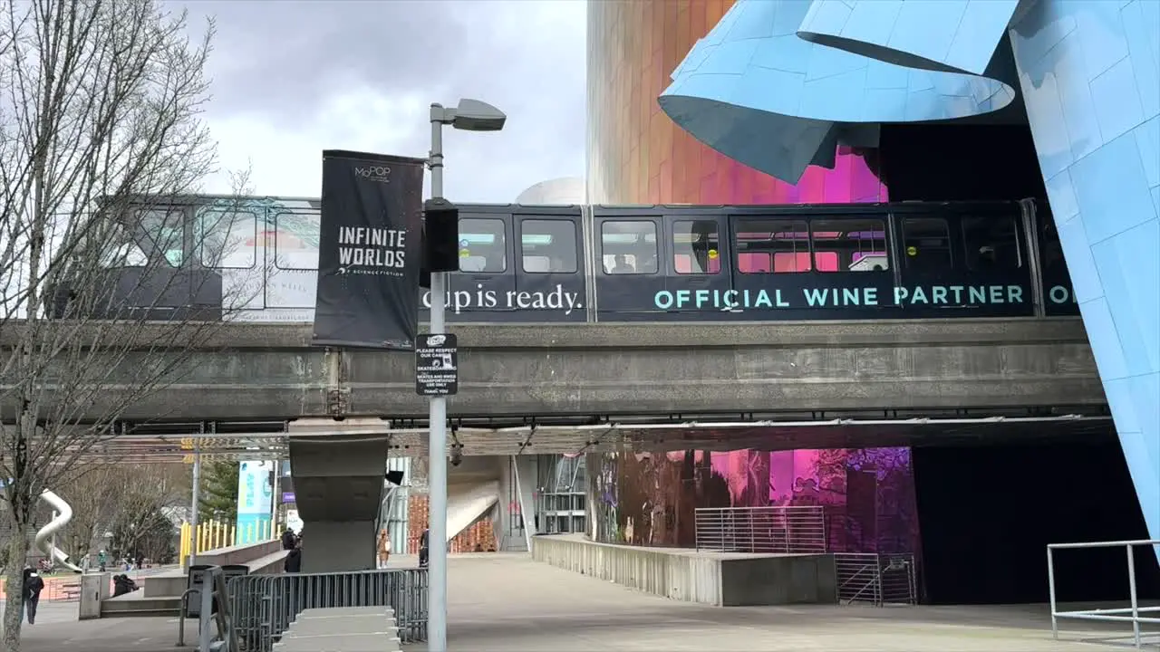 Monorail Passing Through The Museum Of Pop Culture In Seattle With People Walking Past Underneath