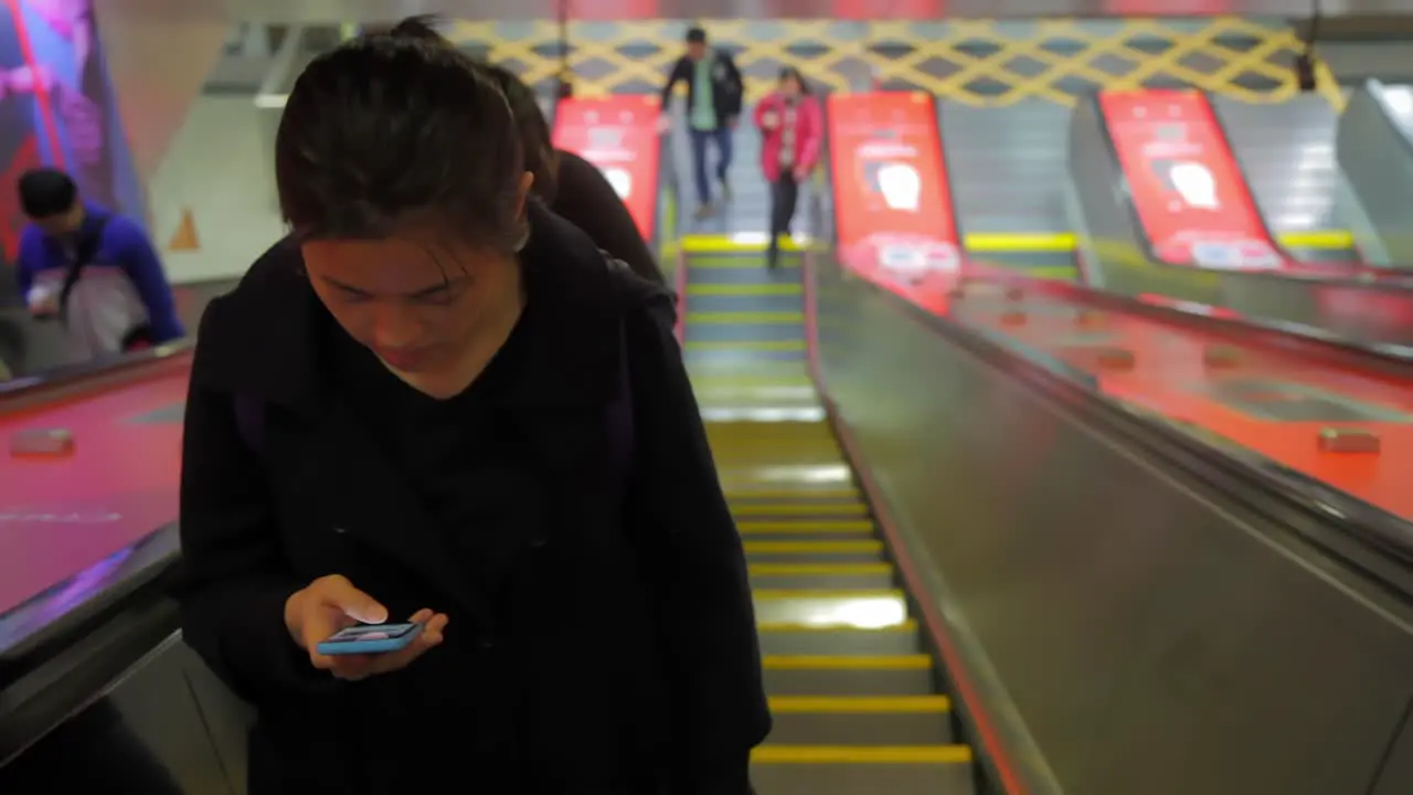 Asian woman looks intently at her phone screen as she climbs the escalator