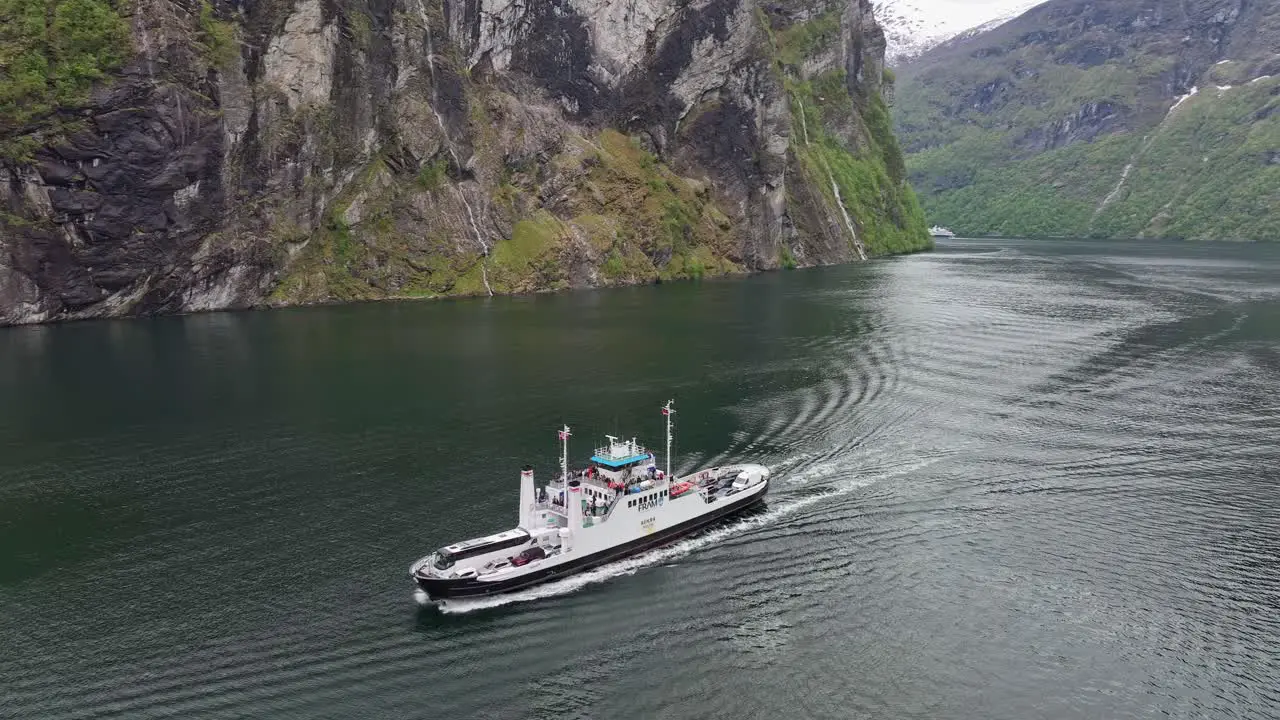 Car and tourist ferry full of people cruising in spectacular Geiranger Fjord Norway Aerial rotating around ship showing all surrounding landscape while keeping ship in middle of frame