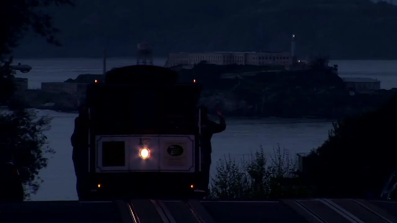 A San Francisco cable car rises over a hill at night