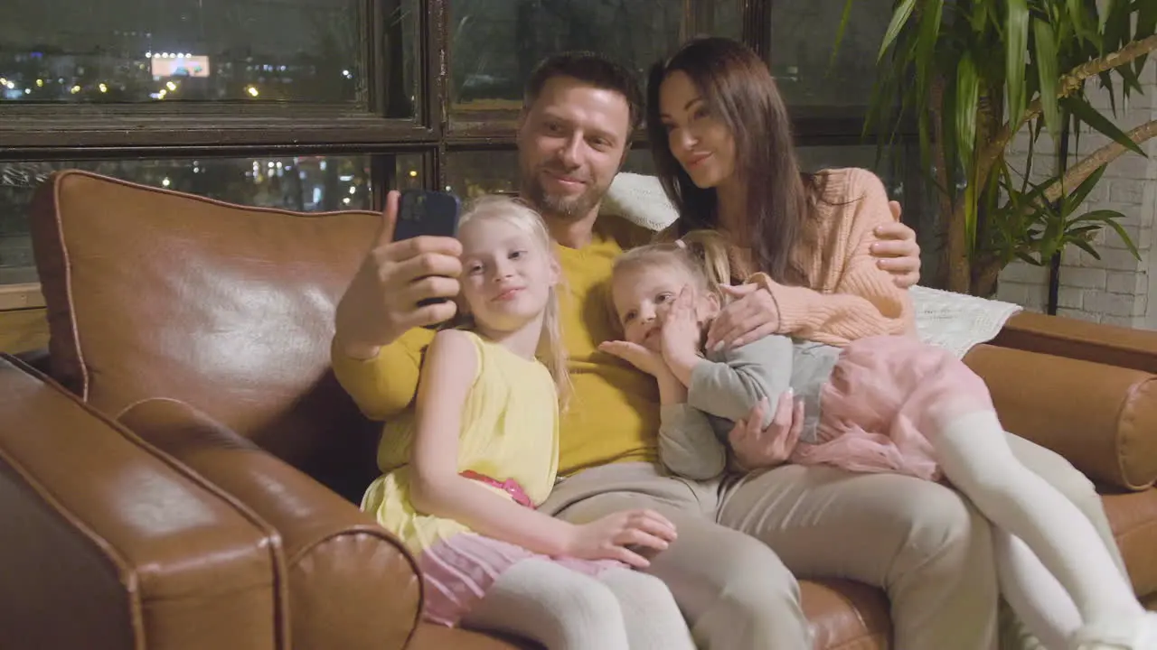 Glückliche Eltern Und Zwei Kleine Mädchen Die Selfie-foto Machen Während Sie Zu Hause Auf Dem Sofa Sitzen