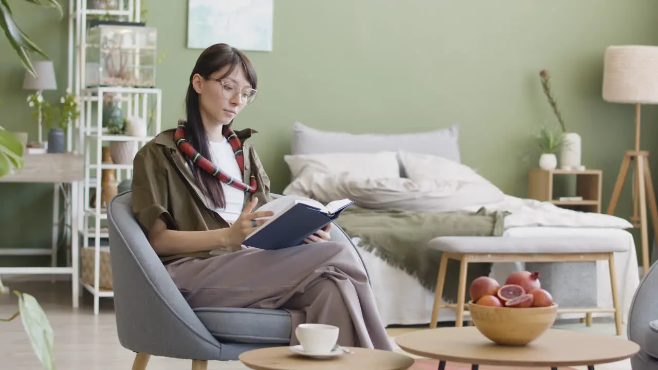 Mujer Joven Con Su Mascota Serpiente Alrededor Del Cuello Leyendo Un Libro Mientras Se Sienta En Un Sillón En Casa