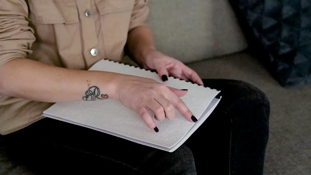 La Cámara Se Enfoca En La Mano De La Mujer Leyendo Un Libro Braille Sentado En El Sofá En Casa 2