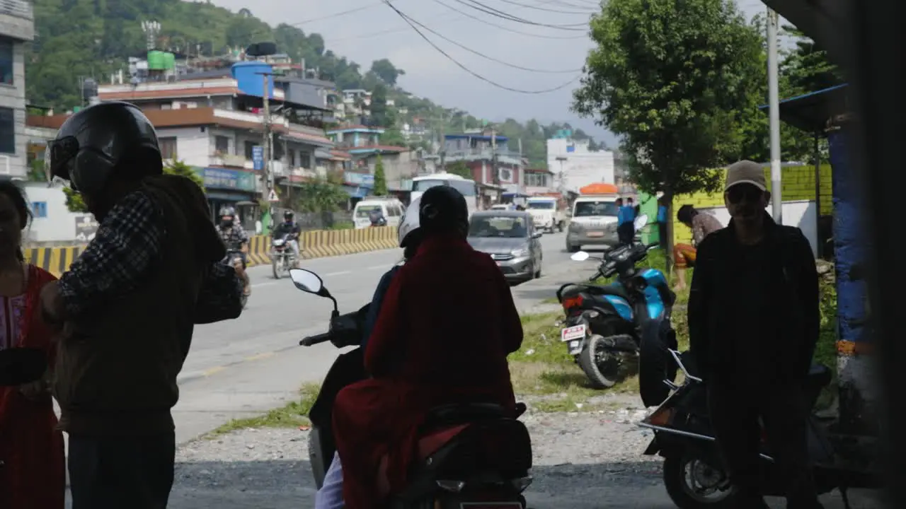 Rear view of Nepalese motorbike taxi drivers waiting in the shade of building silhouettes against village background