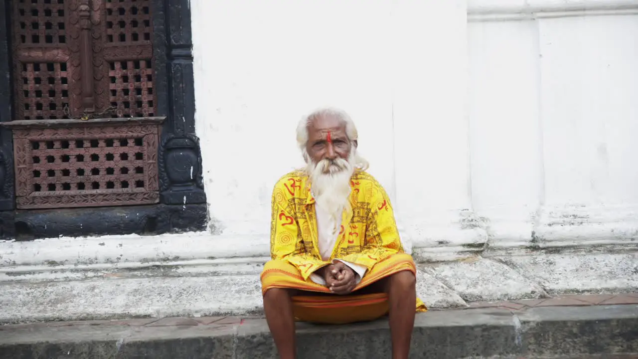 Frontal view of old hermit sacred man in yellow robes against white wall on side of road