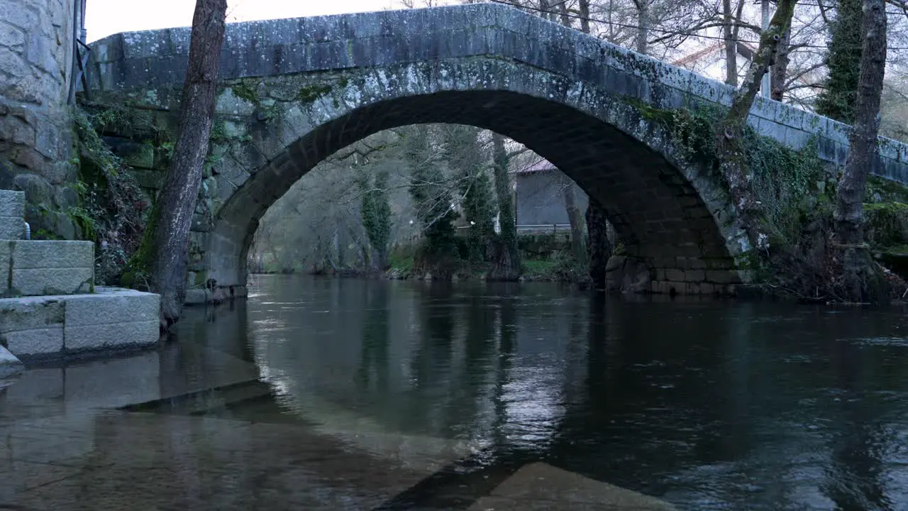 Low angle view of shallow water steps into River Molgas and Roman bridge with arch