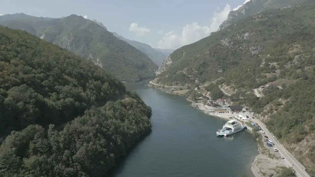 Drone shot flying over the mountains near the Koman lake in Albania on a sunny day with clouds with blue water and a green valley and a ferry dock in sightLOG