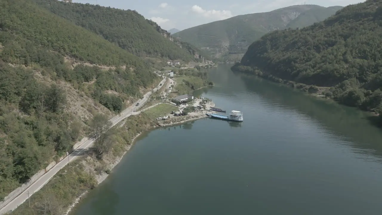 Drone shot flying over the ferry stop in Fierze Albania with a boat and ferry in the water loading passengers on a sunny day LOG