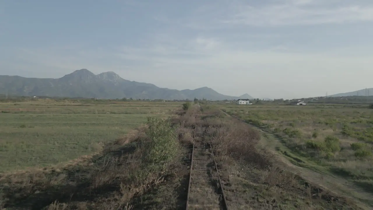 Drone shot that follows old and unused train track in the valley between the mountains in Albania on a cloudy day LOG