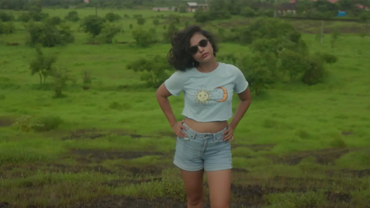 An Indian young woman with stylish sunglasses playfully runs her fingers through her hair in the midst of the serene and natural environment