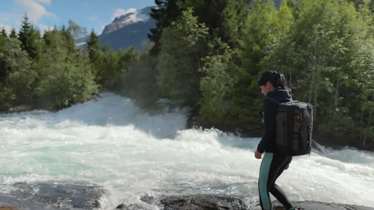 Female traveler with a backpack drinking water in nature in the forest near a mountain river