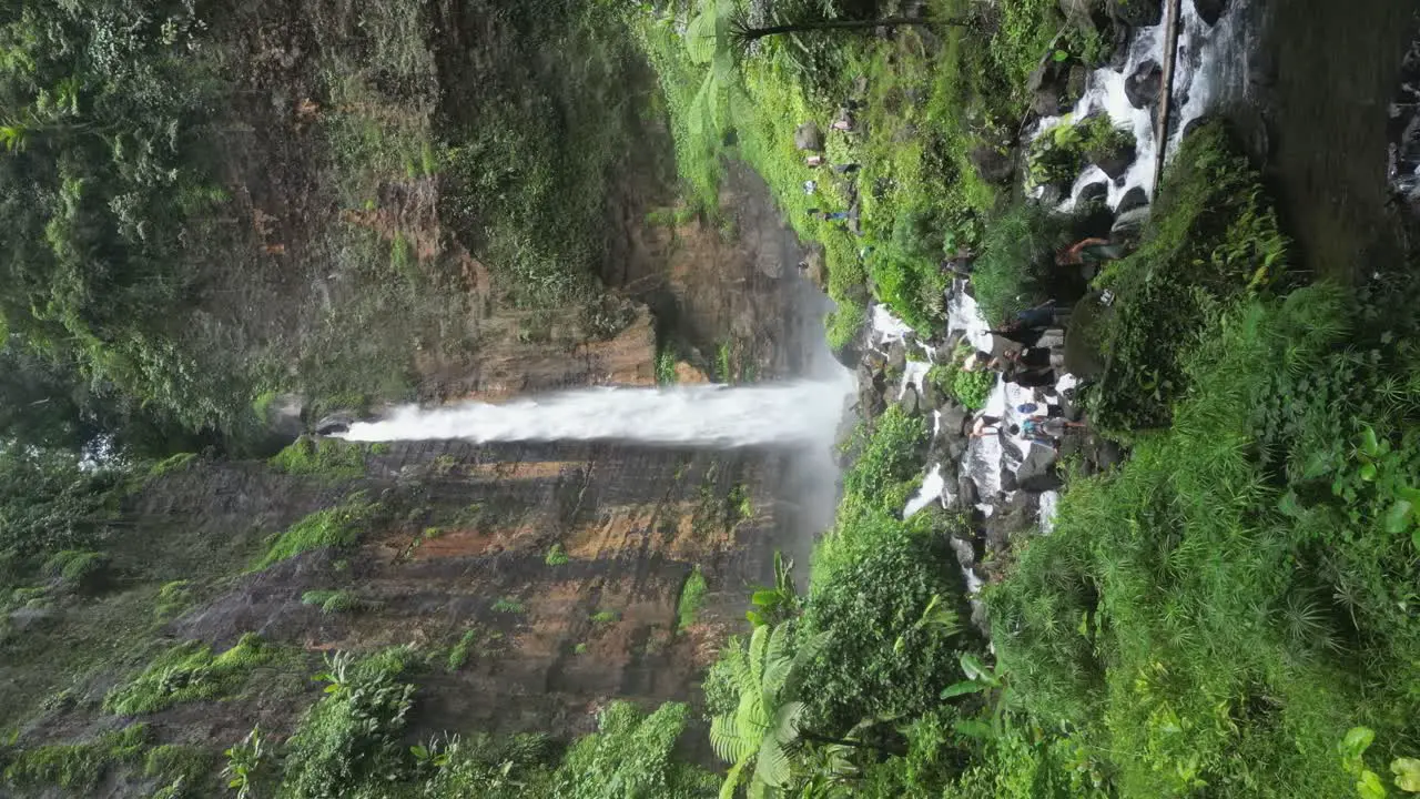 Tourists gather on rugged terrain below Kapas Biru waterfall on Java