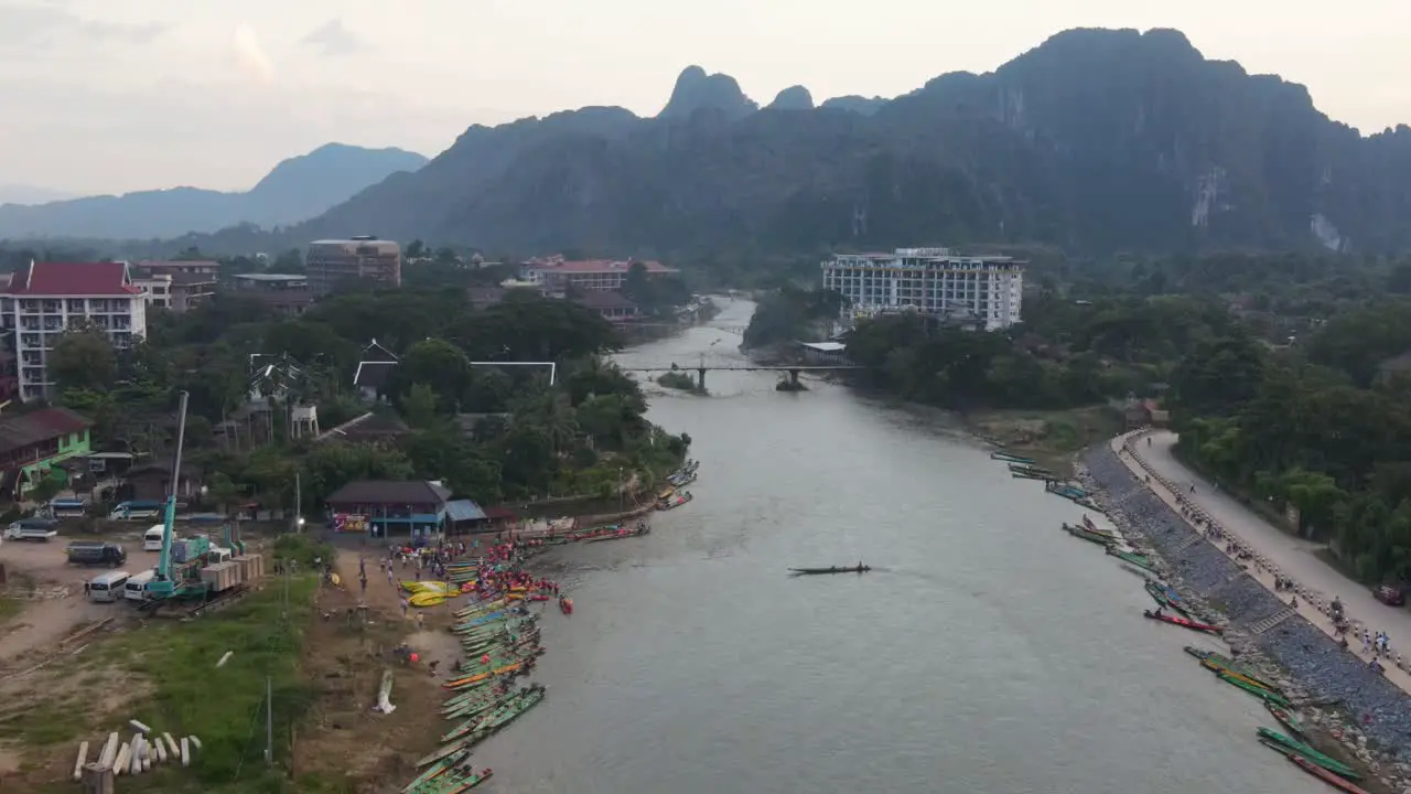 Aerial Flying over Nam Song River At Vang Vieng With Long Boats Moored And Large Ground Crane Parked Nearby