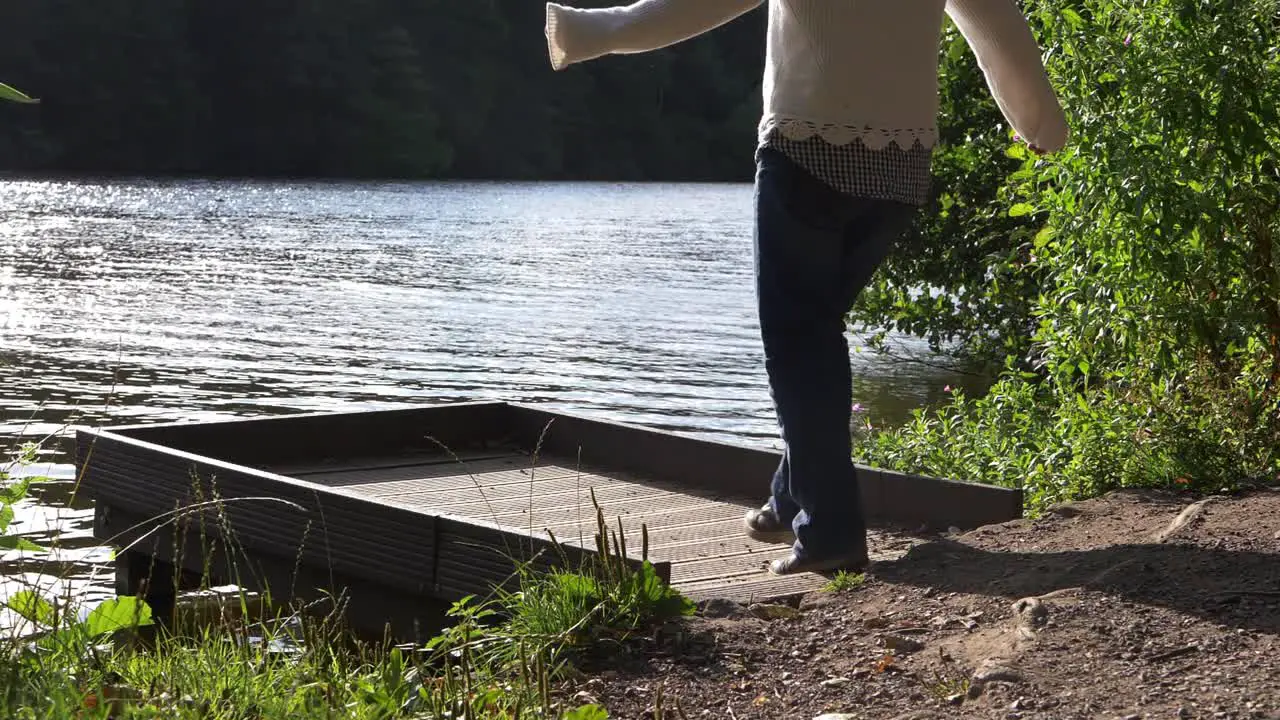 Woman in solitude walks onto pier by lake wide shot