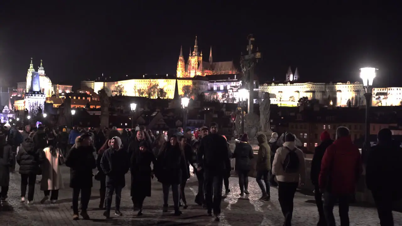 Crowds strolling on Charles bridge at night below Prague castle