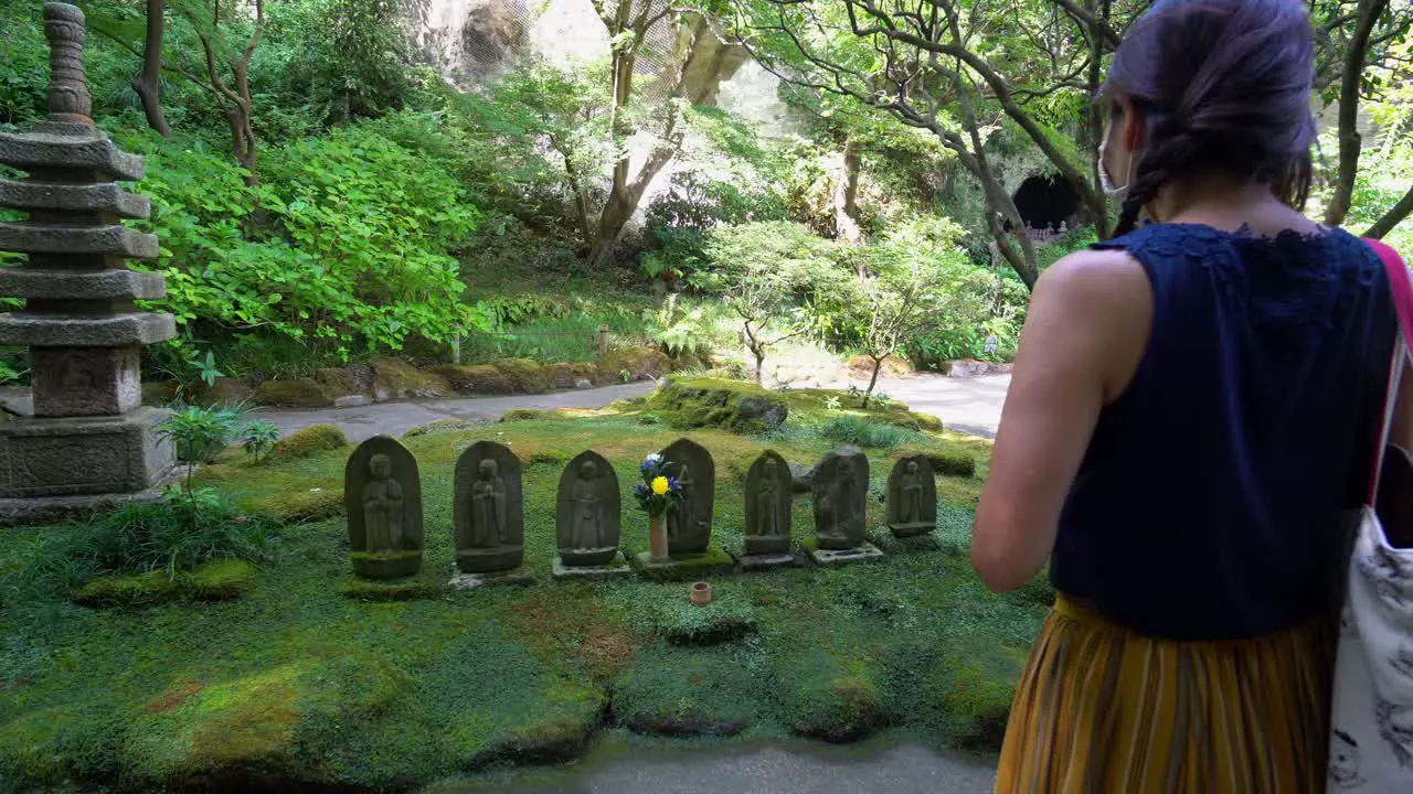 A woman walks through a Kamakura temple in Japan and says a prayer in front of small statues of Buddhas