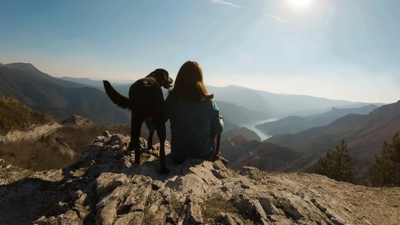 Girl sitting with black labrador dog on a mountain with beautiful lake canyon in the background