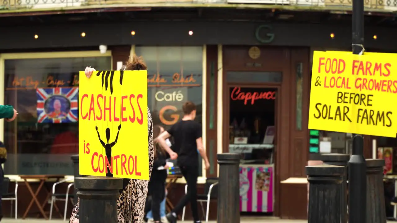 Caucasian woman that is part of the protestant group holding a yellow board sign promoting how cashless society will effect our freedom and the government will be in control of us knowing our expenses