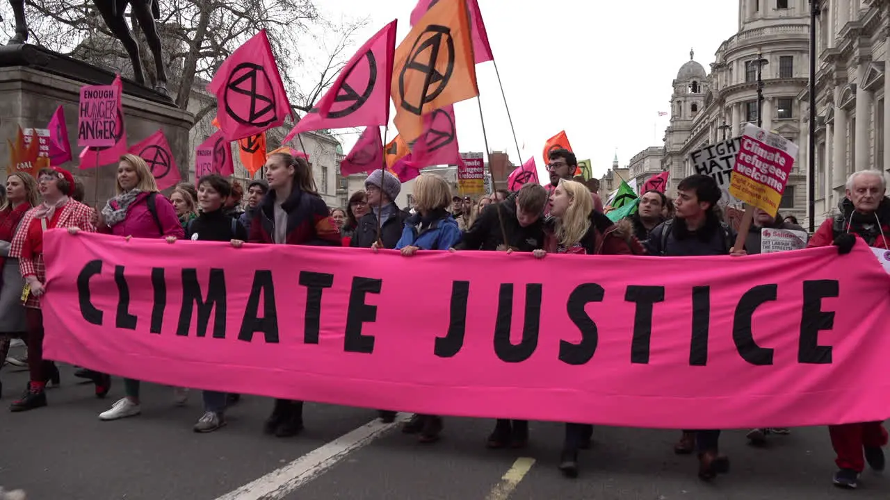 People lead an Extinction Rebellion protest with a large bright pink banner that says Climate Justice”