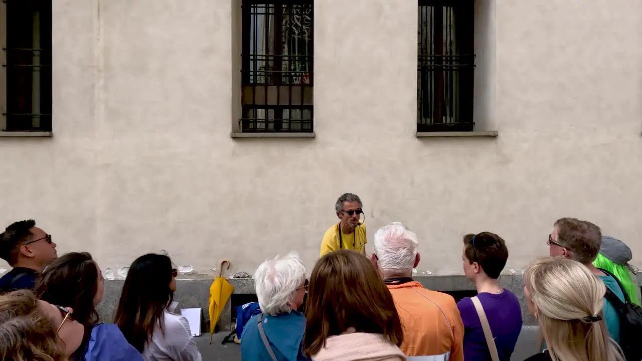 View Behind Tour Group Listening To Energetic Italian Tour Guide Speaking Enthusiastically In Milan Italy