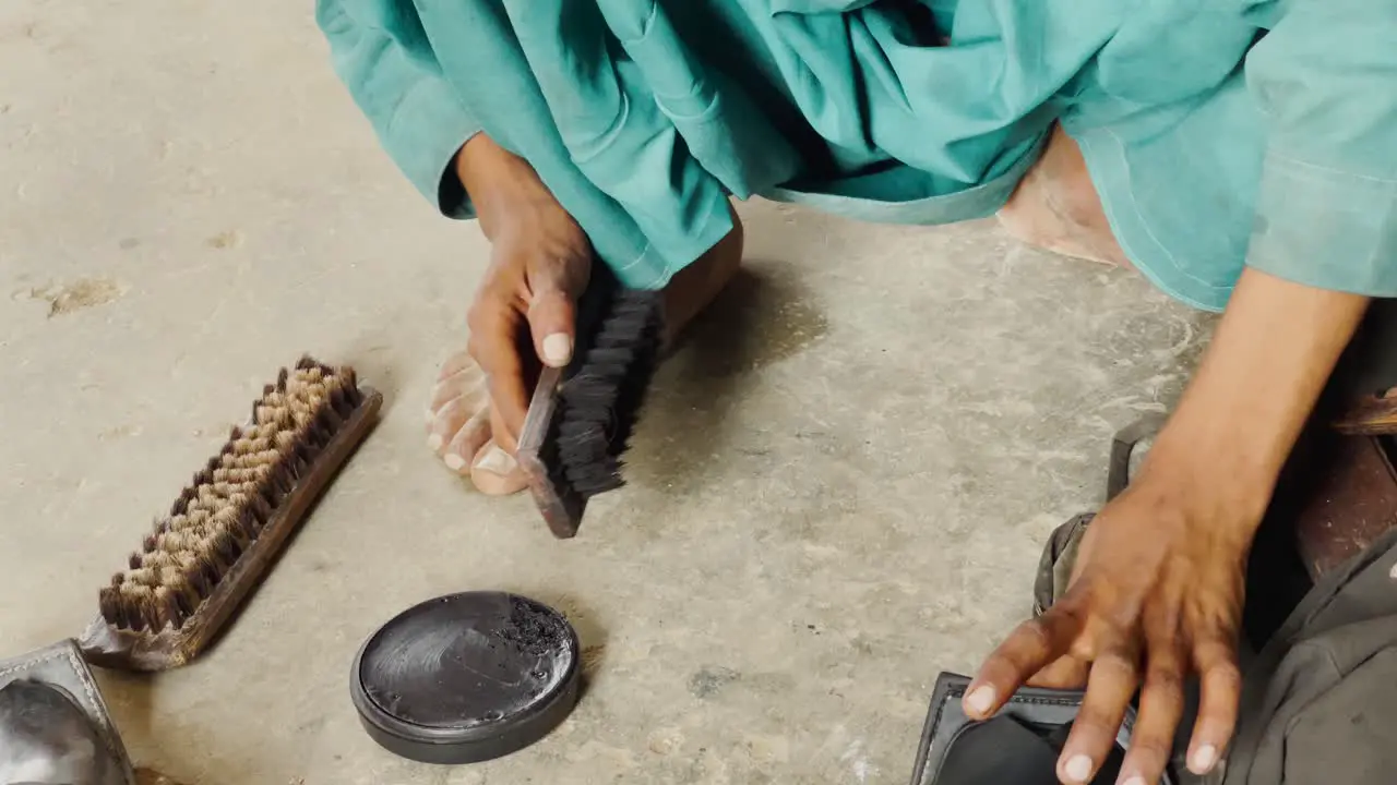 Overhead View Of Young Boy Using Brush To Clean Slippers On Floor In Pakistan