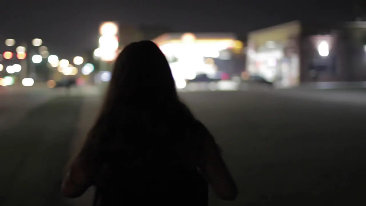 Tracking Shot From Behind A Young Woman With A Blurry Gas Station In The Background