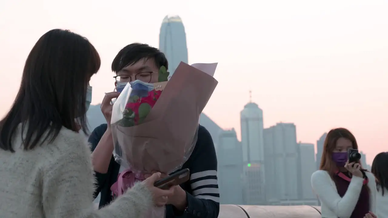 A couple takes photos along the Victoria Harbour waterfront to enjoy the view of the Hong Kong Island skyline while the sunset sets in