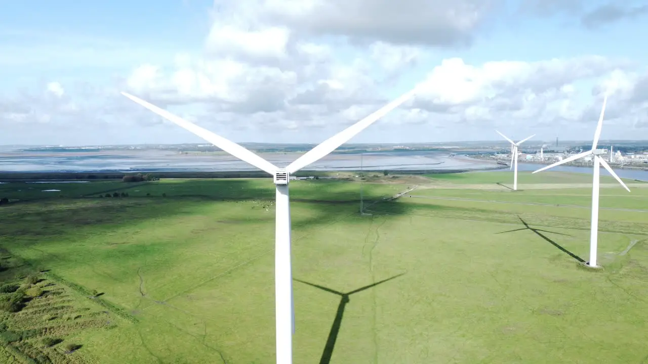 Alternative green energy wind farm turbines spinning in sunny Frodsham Cheshire fields aerial view rising left