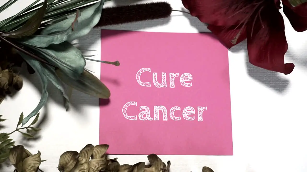 Lay Flat Design- CURE CANCER APPEARS DIGITALLY written on a piece of pink cardstock on a white canvas backdrop with blue green and burgandy floral accents