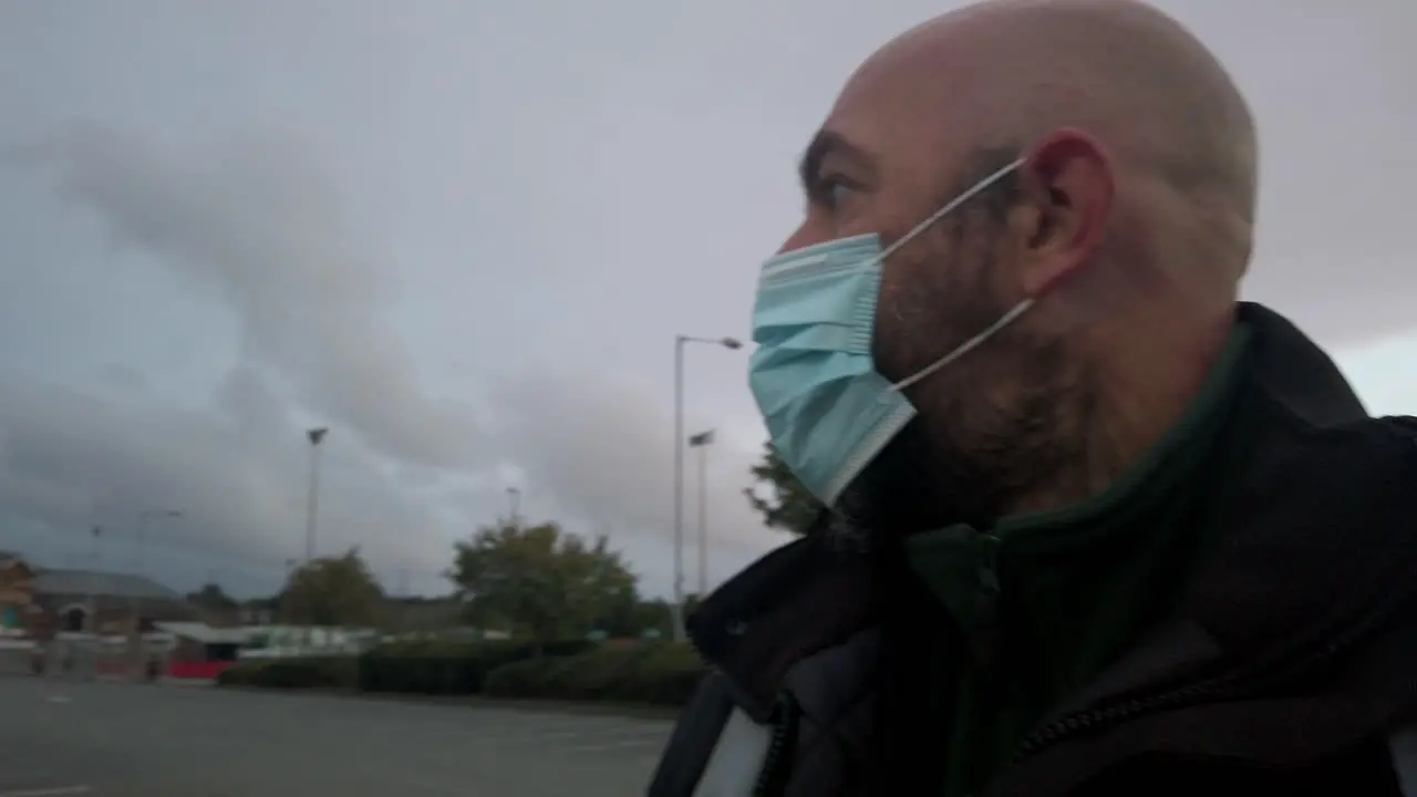 Male in workplace wearing uniform and PPE face mask against corona virus walking car park