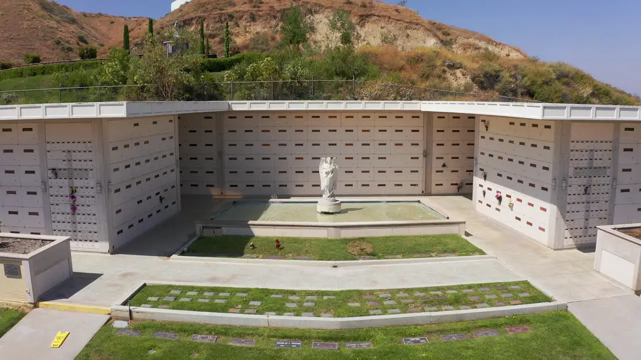 Low push-in aerial shot of a Catholic angel statue in front of a stone mausoleum at a mortuary in California