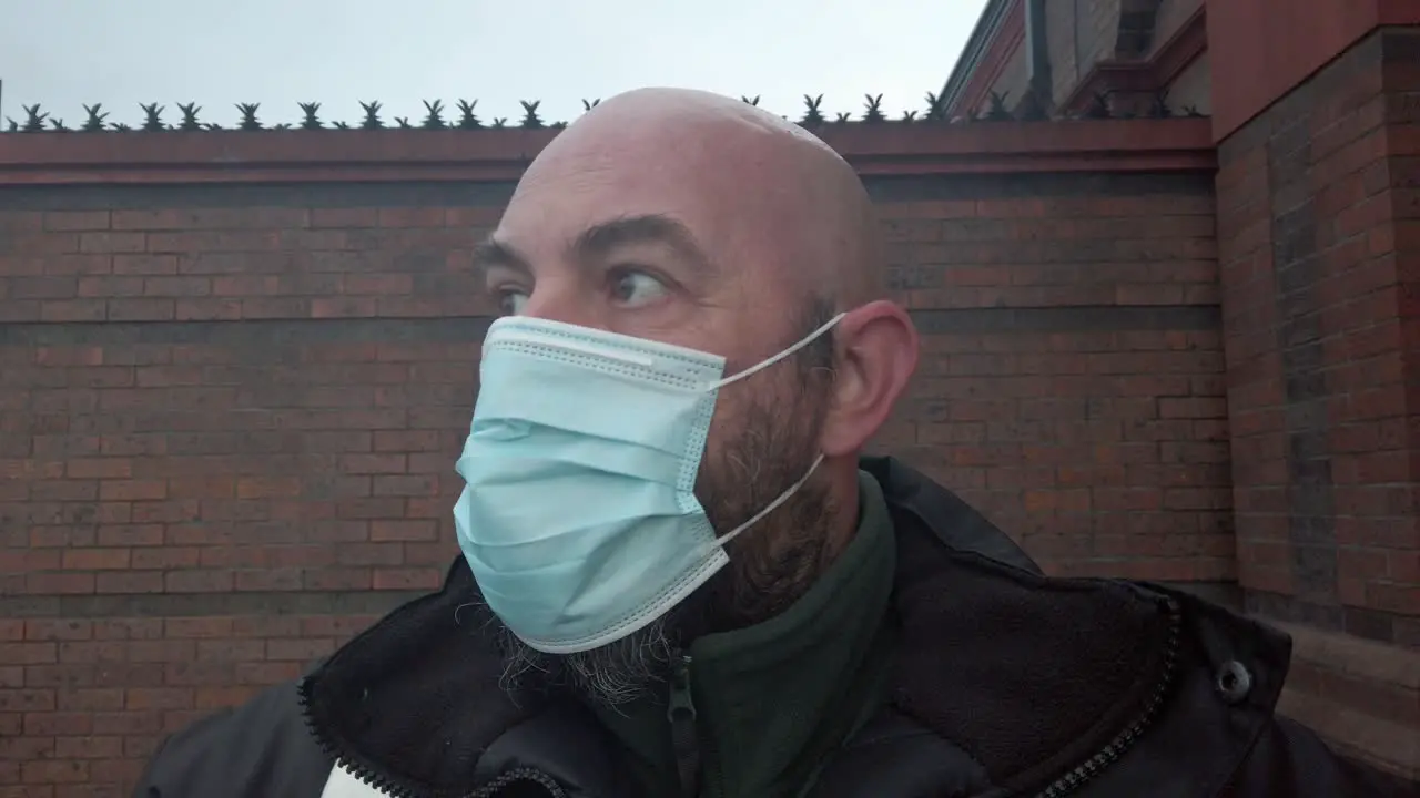 Male security guard fixes protective corona virus medical PPE mask in front of high brick wall