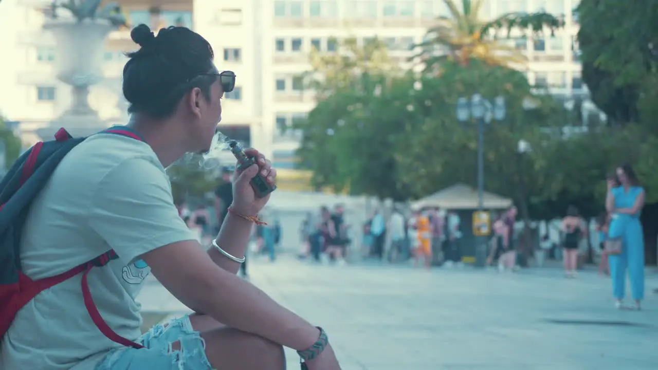 Young man smoking vape while sitting in park Slow Motion