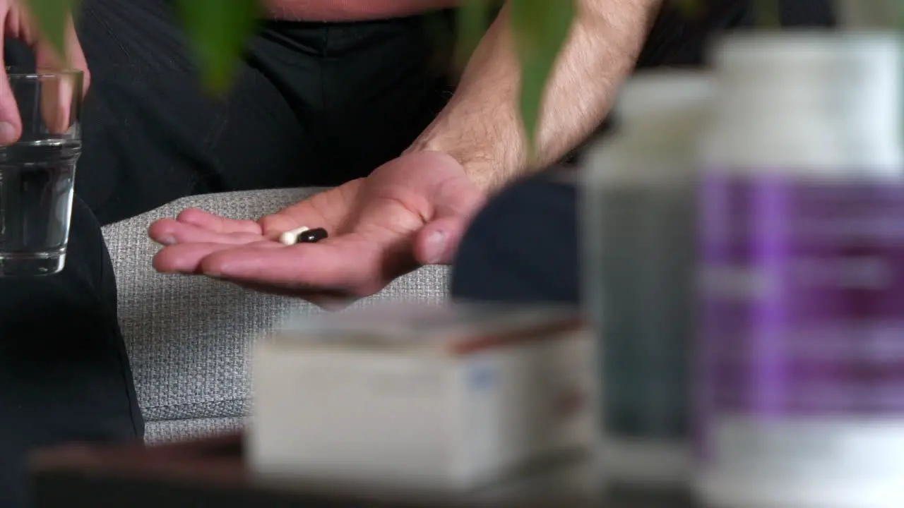 Slide left focus on a man hands holding two pills with a glass of water