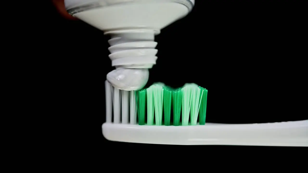 A toothbrush being loaded with some toothpaste dark background